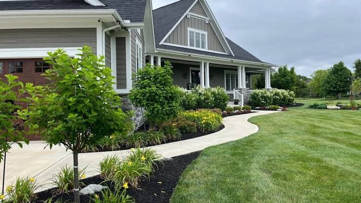 Curved front walkway bordered by dark mulch, flowers, and a striped lawn